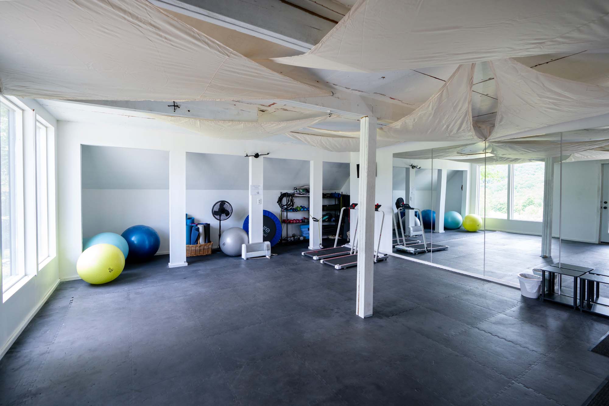 Spacious room with a black rubber floor and white walls. There are large windows on the left side.